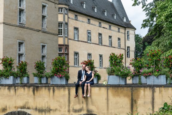 Brautpaar sitzt auf einer Mauer vor einem Schloss