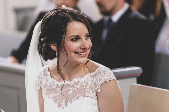 Eine fröhlich lachende Braut mit Schleier schaut zu ihrem Bräutigam.